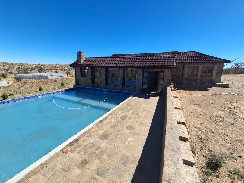 Outdoor pool area featuring a stone-paved patio, stone-clad exterior walls, and a tiled roof, set against a rural landscape.