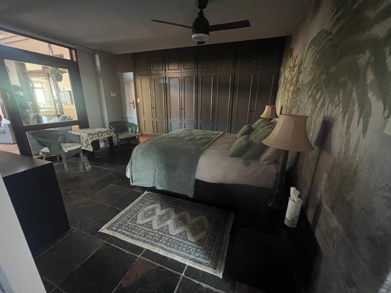Spacious bedroom featuring dark built-in cupboards, tiled flooring, a ceiling fan, and large glass sliding doors providing natural light and access to the patio.