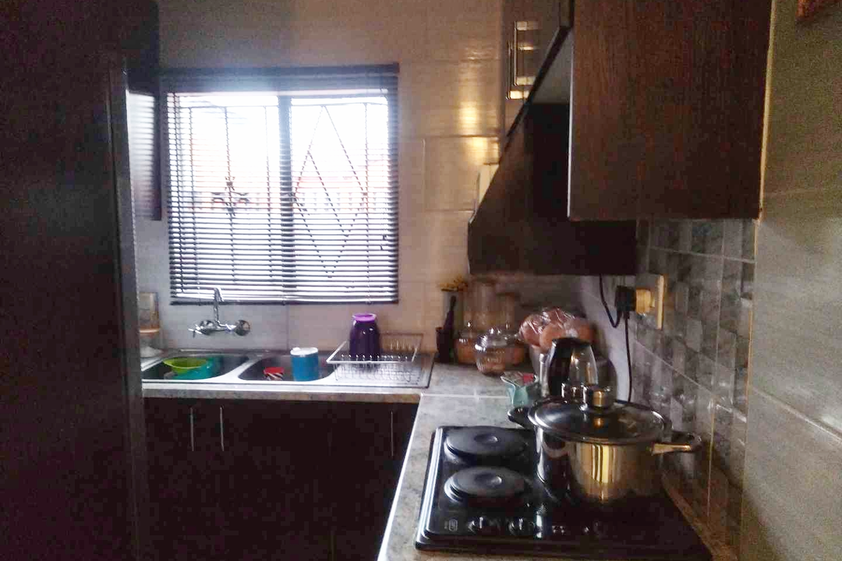 A compact kitchen featuring dark cabinetry, a built-in electric hob, a stainless steel double sink, and tiled splashbacks.