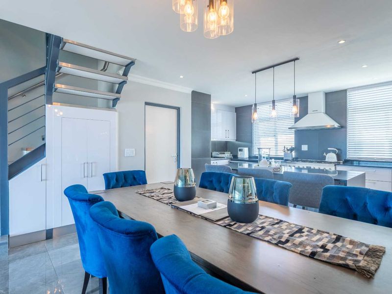 Modern open-plan living and dining area featuring a sleek kitchen with integrated appliances, stone countertops, and a contemporary staircase with glass balustrades.