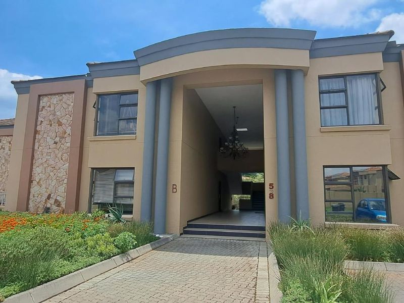 Front elevation of a modern apartment complex featuring stone cladding, paved driveway, and a covered entrance with architectural columns.