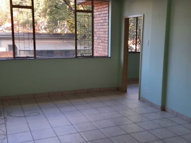 An empty living room featuring tiled flooring and a large window with security bars, providing natural light and access to adjacent rooms.