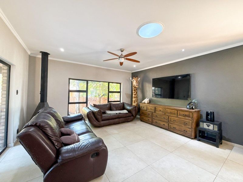 Spacious living room featuring large format floor tiles, a modern freestanding fireplace, ceiling fan, and a circular skylight providing natural light.
