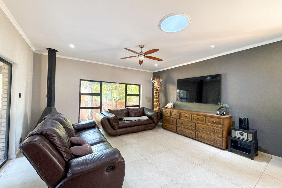Spacious living room featuring large format floor tiles, a modern freestanding fireplace, ceiling fan, and a circular skylight providing natural light.
