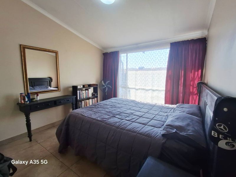 A bedroom featuring tiled flooring and a large window with security gate, providing natural light and access to the exterior.