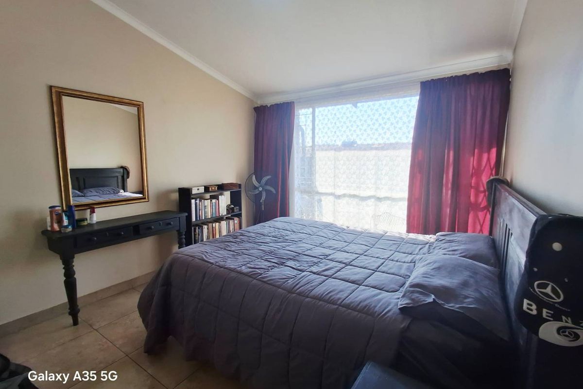 A bedroom featuring tiled flooring and a large window with security gate, providing natural light and access to the exterior.