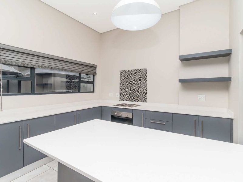 Modern kitchen featuring grey cabinetry, white stone countertops, a central island, built-in oven, hob, and mosaic tile splashback.