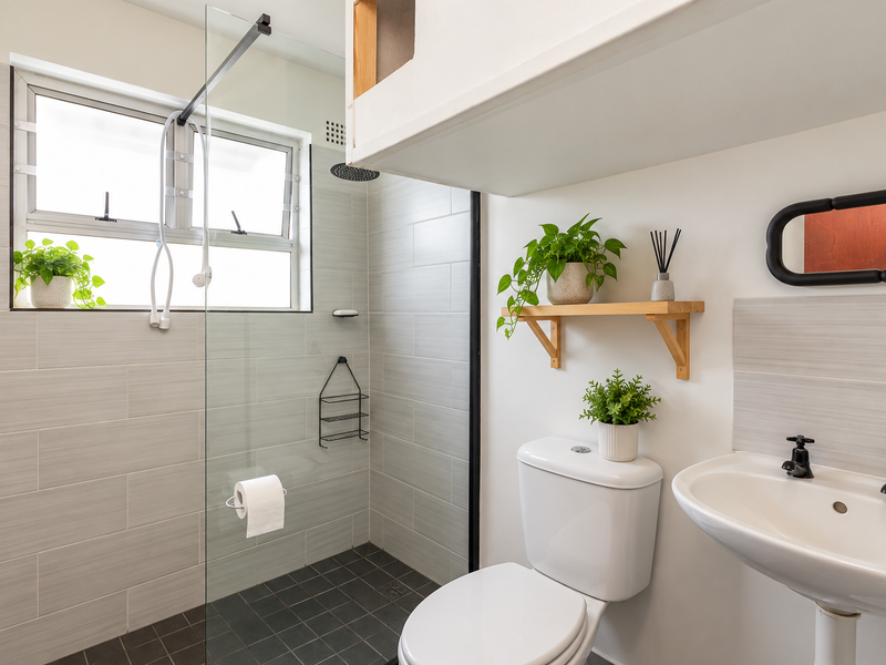 A modern bathroom featuring a glass-enclosed shower with a rain shower head, a wall-mounted basin, and a clean, tiled finish.