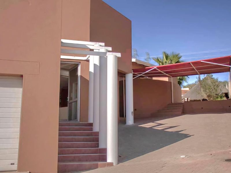 Front exterior view of the property featuring a garage, paved driveway, covered patio area with a pergola, and concrete entrance stairs.