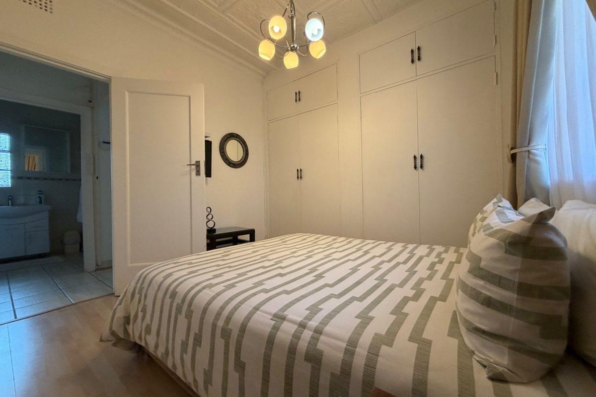A well-maintained bedroom featuring classic pressed metal ceilings, built-in storage cupboards, and direct access to an adjoining bathroom.