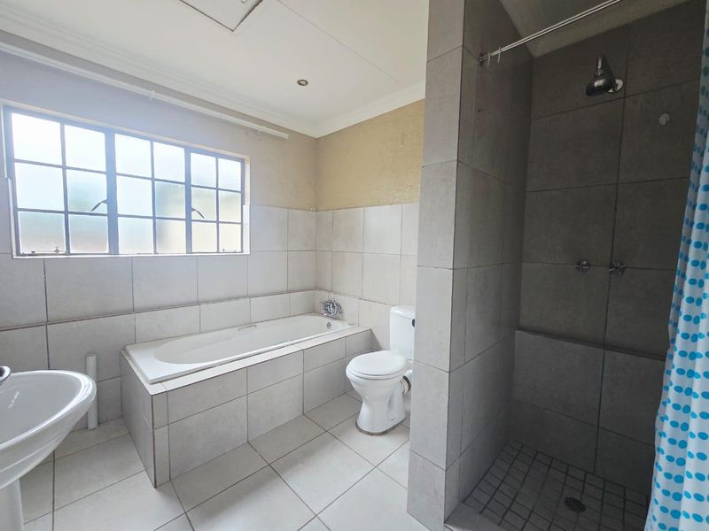 A functional bathroom featuring a built-in bathtub, separate shower enclosure, pedestal sink, and toilet, with neutral tiling throughout.