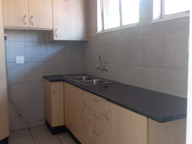 A functional kitchen featuring light wood-tone cabinetry, dark laminate countertops, a stainless steel sink, and neutral tiled flooring and backsplash.