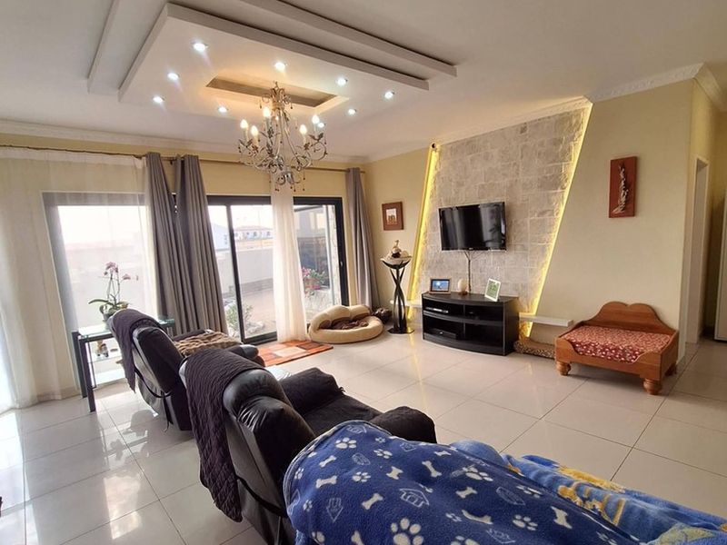 Spacious living room featuring a stone accent wall with integrated LED lighting, a decorative recessed ceiling with downlights, and large sliding glass doors.