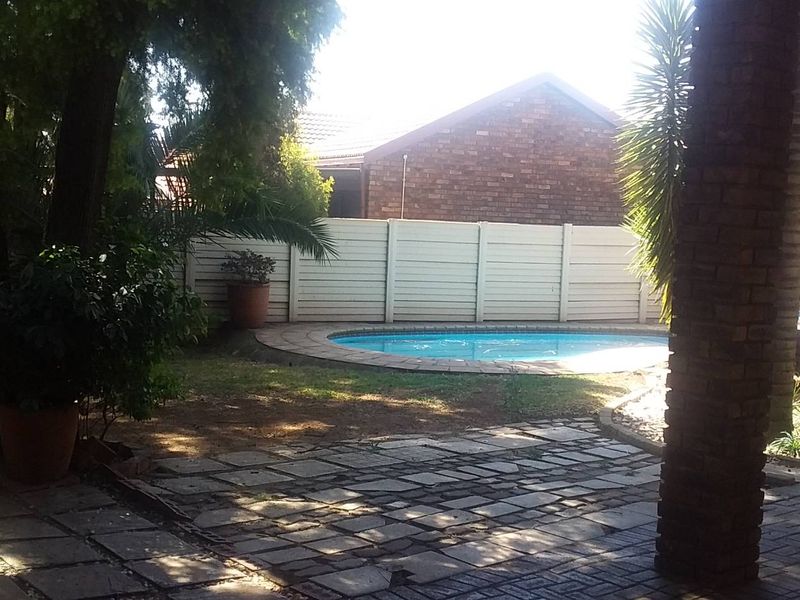 Outdoor entertainment area featuring a swimming pool, paved patio, and a covered thatched structure, set within a private garden with boundary walls.
