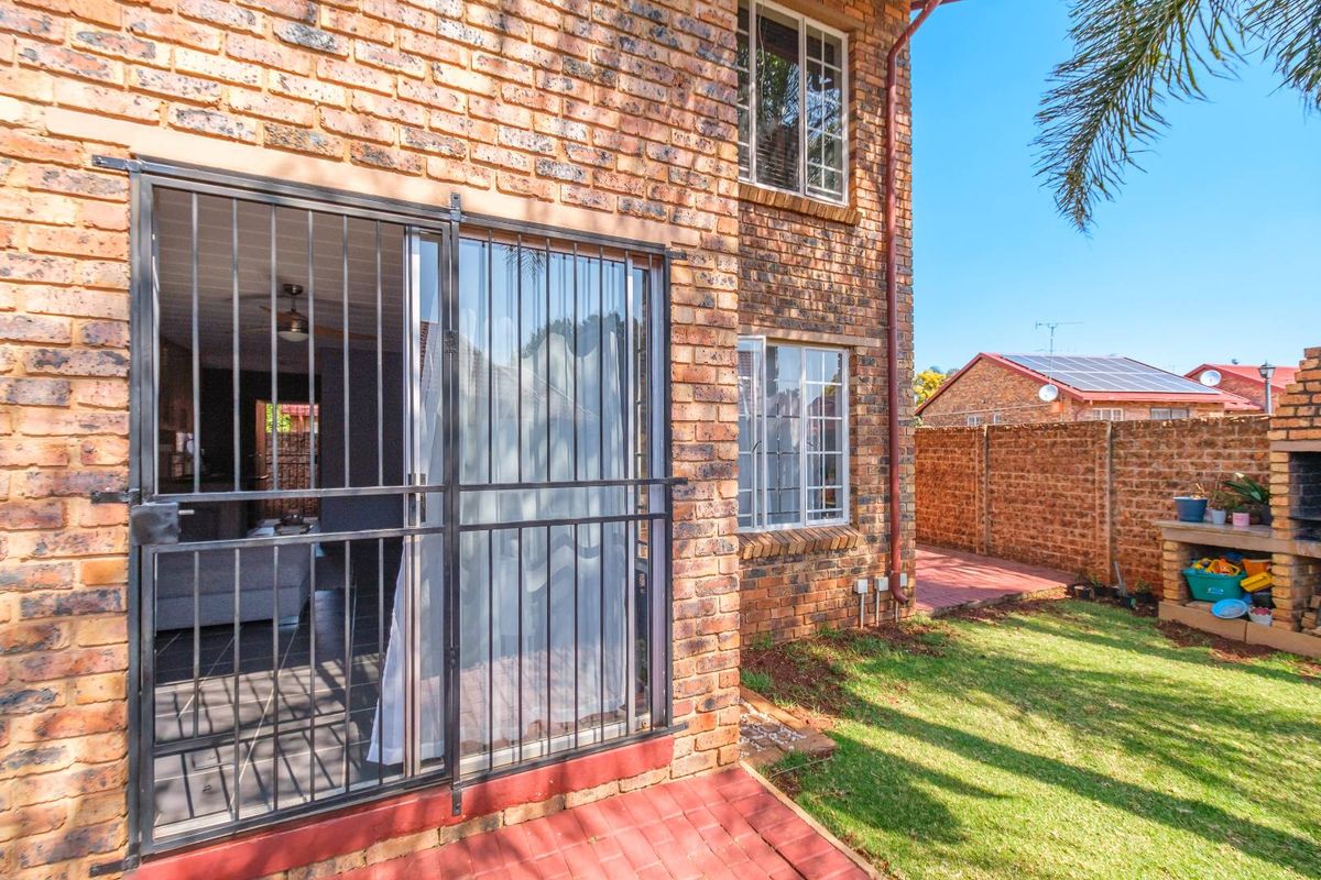 Rear exterior view of the apartment featuring a face brick facade, paved patio area, and a built-in braai, overlooking a small private garden.