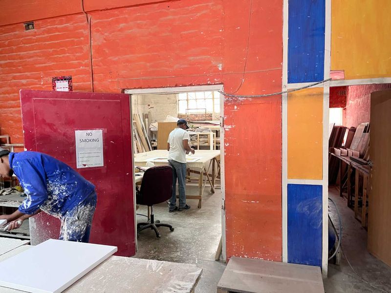 Industrial workshop space featuring exposed brick walls, a heavy-duty steel door, and functional work areas suitable for manufacturing or craft activities.