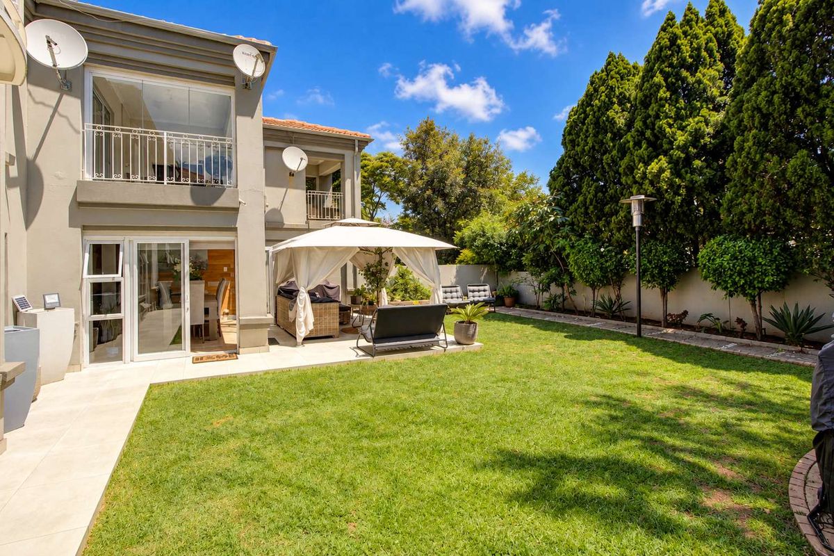 A well-maintained rear townhouse exterior featuring a tiled patio, landscaped garden, and a balcony with wrought iron railings.