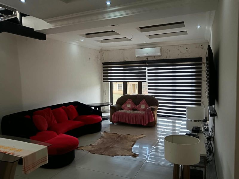 Spacious living room featuring tiled flooring, recessed ceiling lighting, and a wall-mounted air conditioning unit, currently showing signs of wall surface deterioration.