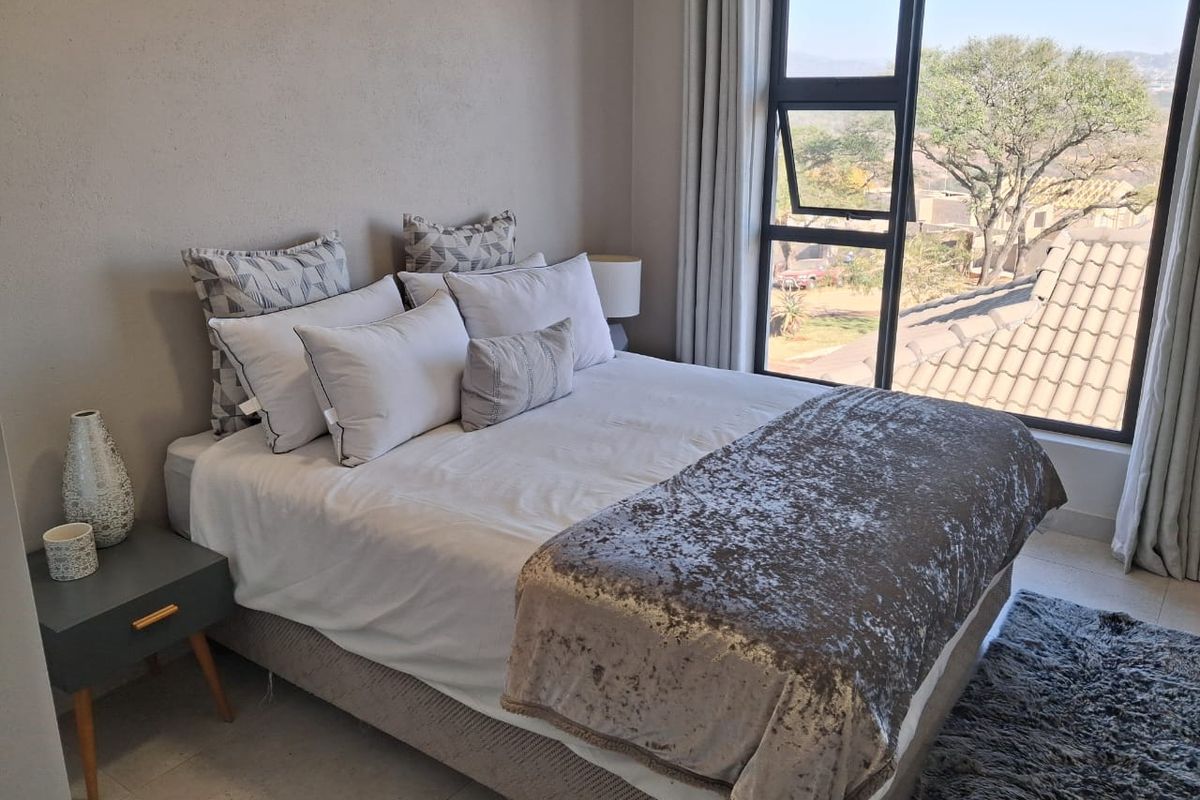 A well-maintained bedroom featuring neutral wall tones, tiled flooring, and a large window providing natural light and scenic views.