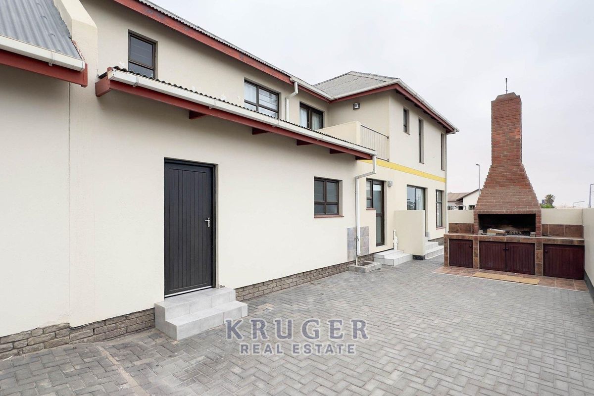 Rear exterior view of the townhouse featuring a paved courtyard, built-in brick braai area, and access doors to the main dwelling.