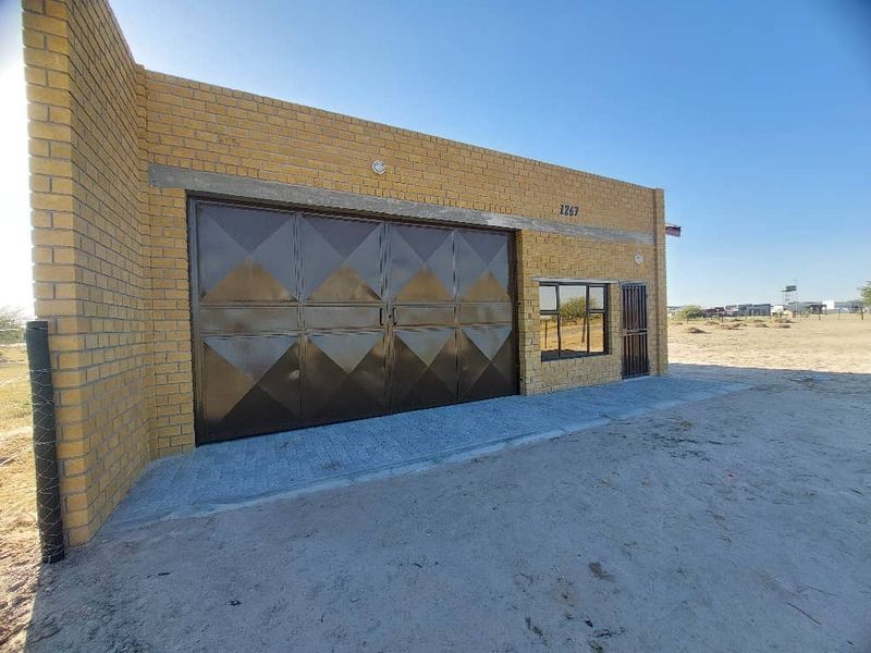 Front view of an industrial-style building featuring a large metal garage door, security gate, and face brick exterior with a paved apron.