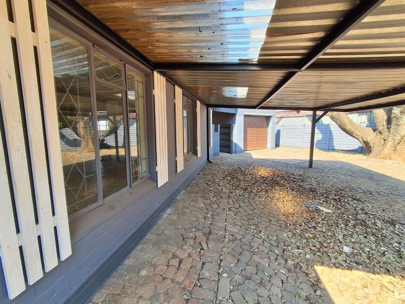 A covered outdoor patio area featuring cobblestone paving, steel roofing, and access to the main house and garage.