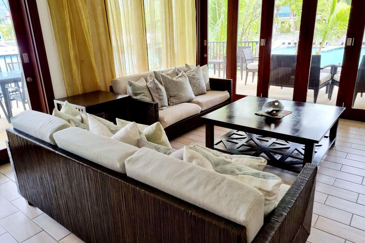 A bright living room featuring large glass sliding doors that open onto a patio area with pool views, finished with tiled flooring.