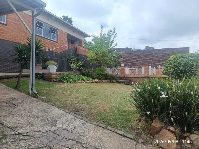 Rear garden area featuring a brick facade, concrete driveway, and tiered landscaping with a retaining wall and metal security fencing.