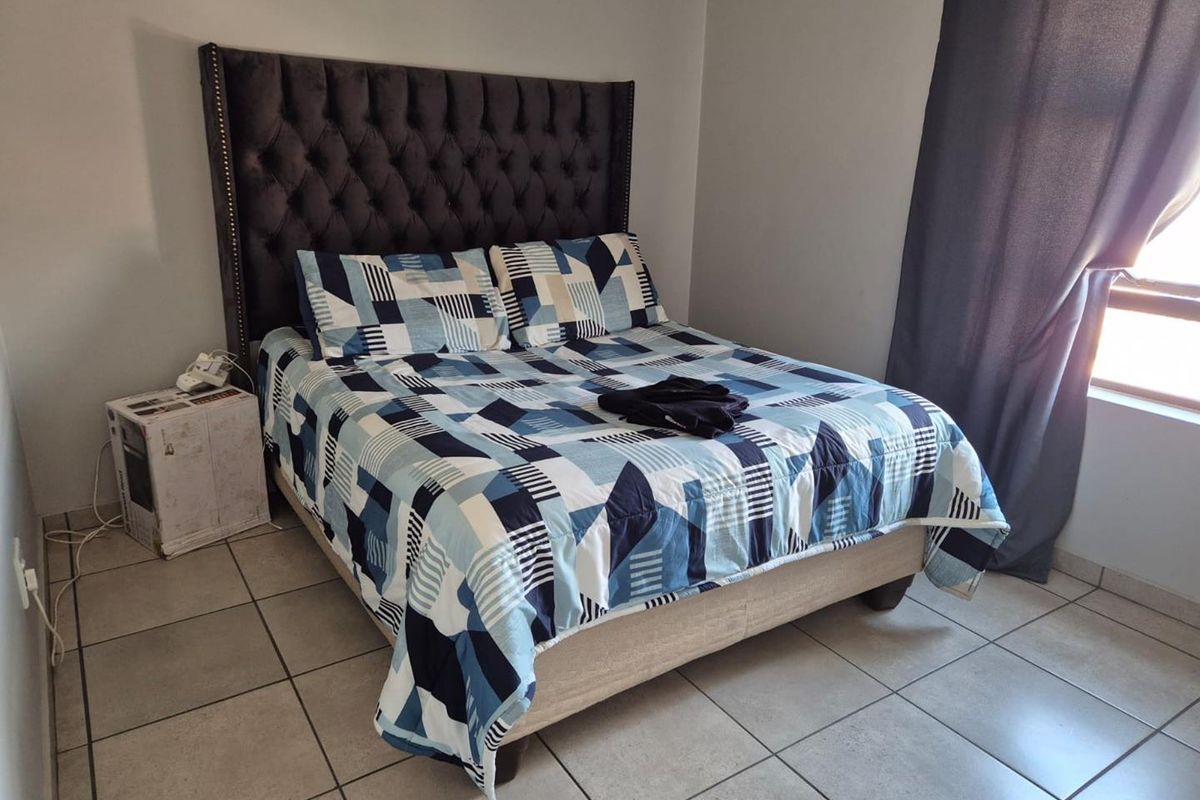 A bedroom featuring neutral wall finishes and tiled flooring, with a window providing natural light and fitted curtain tracks.