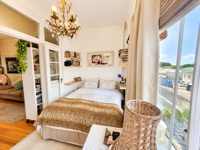 A bright bedroom featuring built-in shelving, a classic chandelier, and large glass sliding doors that open onto a balcony with neighborhood views.