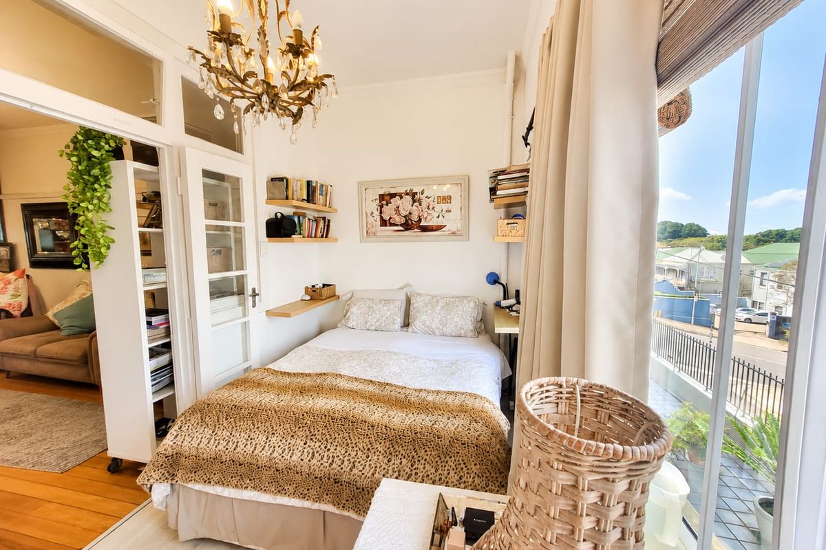 A bright bedroom featuring built-in shelving, a classic chandelier, and large glass sliding doors that open onto a balcony with neighborhood views.
