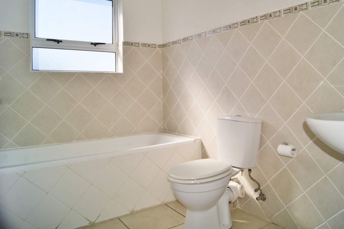 A functional bathroom featuring a bathtub, toilet, and wall-mounted basin with neutral diamond-patterned wall tiles and tiled flooring.