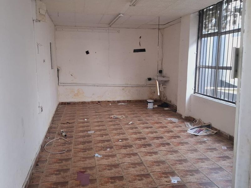 An empty utility space featuring tiled flooring, a wall-mounted basin, and security bars on the window, requiring significant cosmetic refurbishment and repairs.