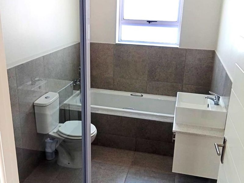 A clean, modern bathroom featuring a bathtub, separate shower enclosure, wall-mounted vanity with basin, and neutral floor-to-ceiling tiling.