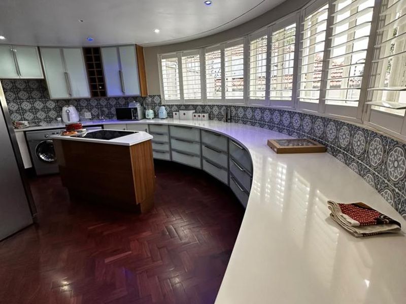 A modern kitchen featuring unique curved cabinetry, stone countertops, patterned tile backsplash, and elegant herringbone hardwood flooring with integrated appliances.