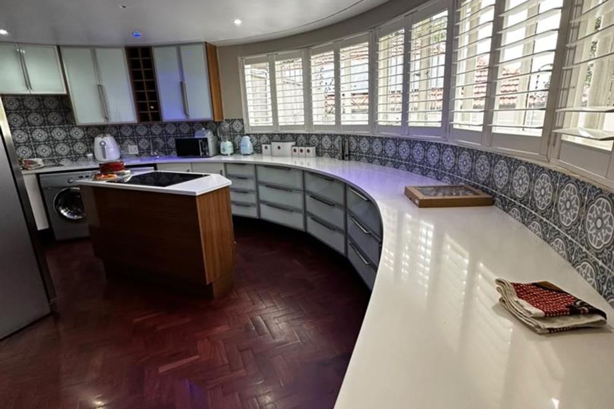 A modern kitchen featuring unique curved cabinetry, stone countertops, patterned tile backsplash, and elegant herringbone hardwood flooring with integrated appliances.