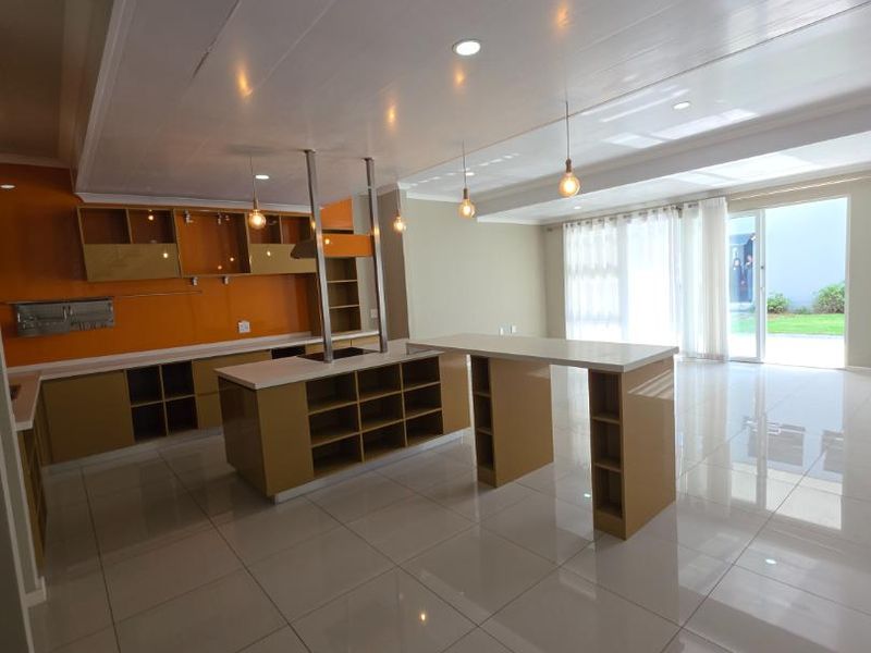 Spacious open-plan kitchen and living area featuring modern cabinetry, a large central island with breakfast bar, and bright tiled flooring leading to the patio.