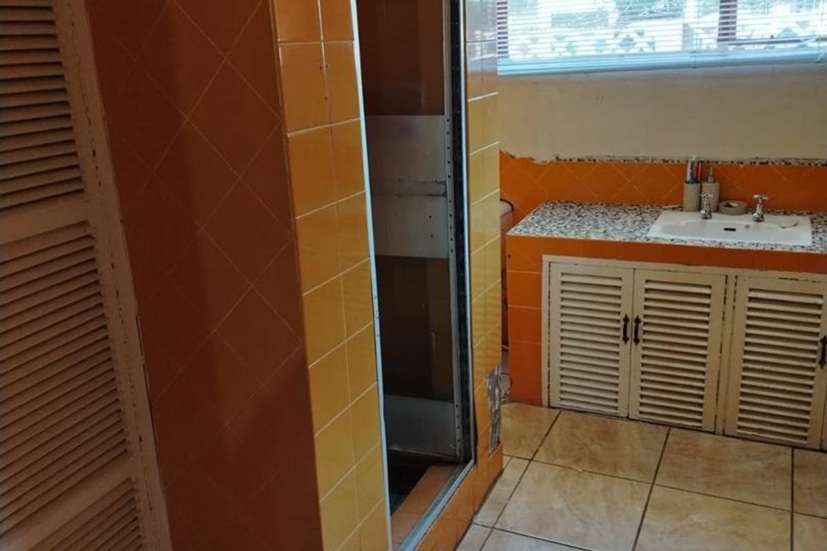 A dated bathroom featuring orange wall tiles, a built-in vanity with storage cupboards, and a shower enclosure requiring maintenance.