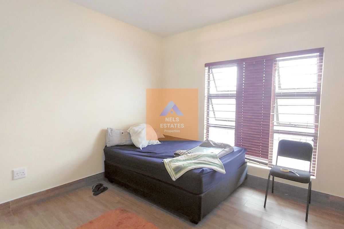 A bedroom featuring wood-look flooring and large windows with fitted blinds, providing natural light.