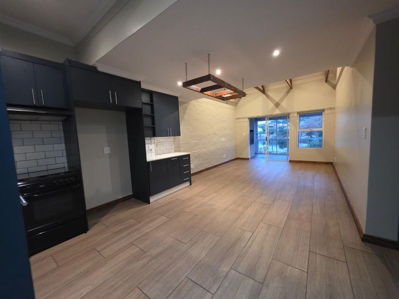 Spacious open-plan living and kitchen area featuring dark cabinetry, subway tile backsplash, exposed timber beams, and sliding doors leading to a balcony.