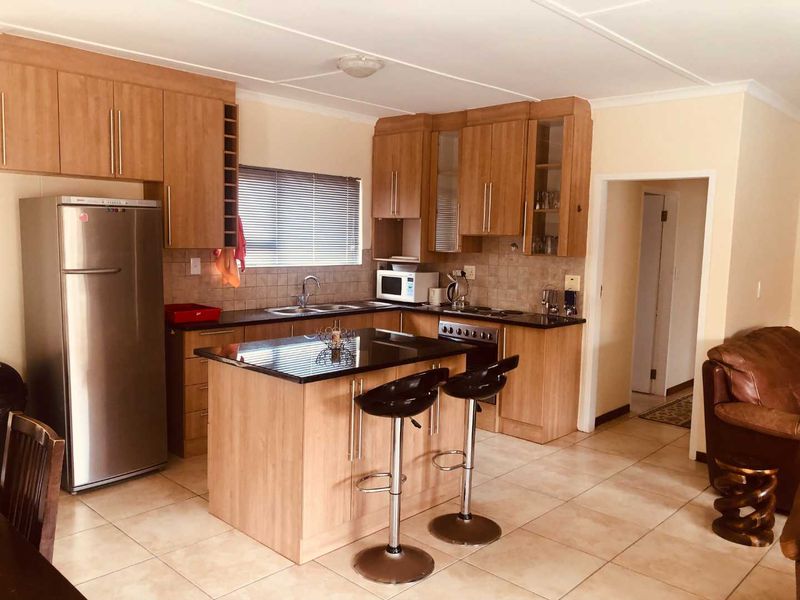 A functional kitchen featuring light wood cabinetry, granite countertops, a central island with breakfast bar seating, and tiled flooring.