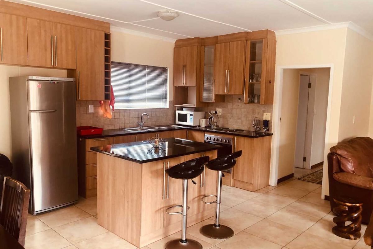 A functional kitchen featuring light wood cabinetry, granite countertops, a central island with breakfast bar seating, and tiled flooring.