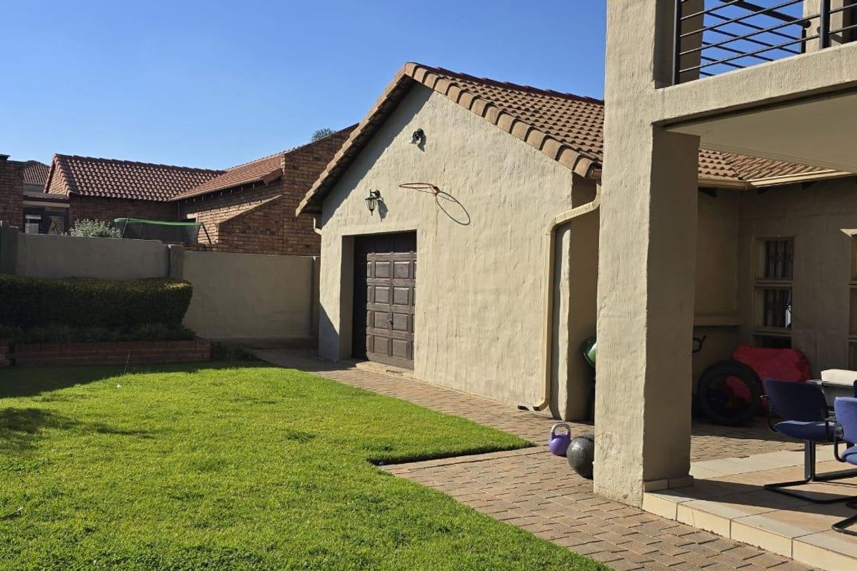 A view of the rear garden featuring a paved patio area, a lawn, and a detached garage structure with a tiled roof.