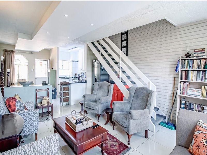 Open plan living area featuring a staircase, tiled flooring, and a connected kitchen space with neutral finishes.