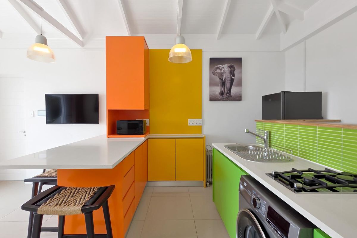 Modern kitchen featuring vibrant multi-colored cabinetry, stone countertops, a gas hob, and a stainless steel sink, set under a high exposed beam ceiling.