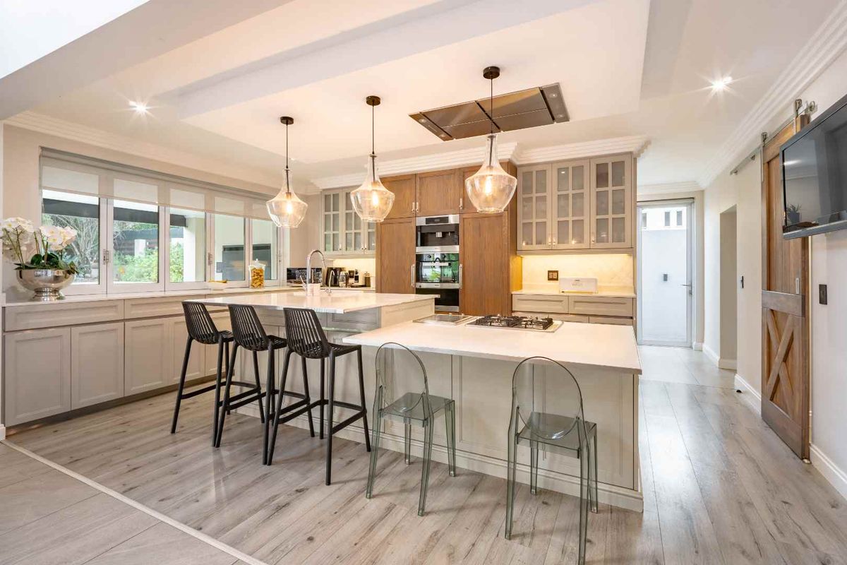 Modern kitchen featuring a large central island, stone countertops, built-in oven, gas hob, extractor fan, and custom cabinetry with integrated lighting.