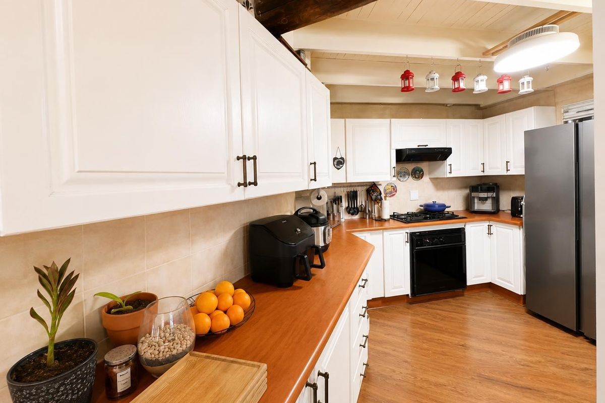 A well-maintained kitchen featuring white cabinetry, warm wooden countertops, a gas hob, and exposed timber ceiling beams, offering a cozy and functional workspace.