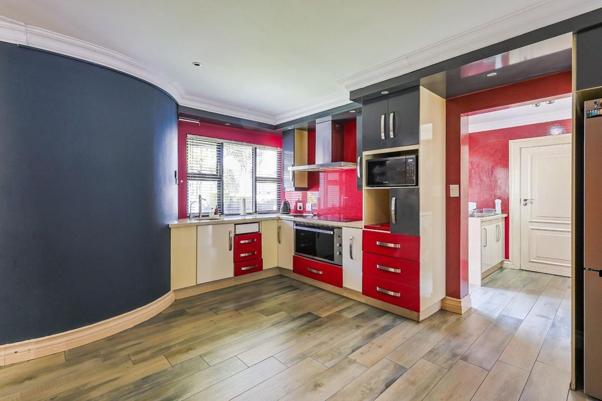 A compact kitchen featuring high-gloss red and cream cabinetry, integrated oven, extractor fan, and wood-look flooring, with an adjacent scullery area.