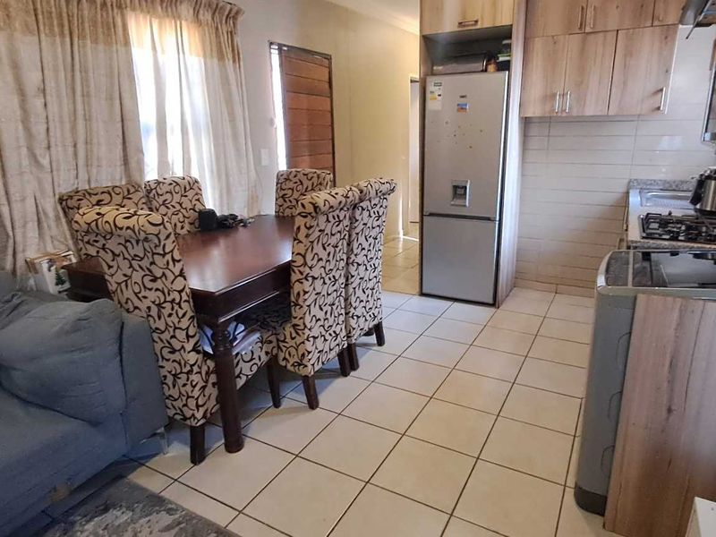 Open-plan living and dining area featuring tiled flooring and a functional kitchen with built-in cabinetry and integrated appliances.