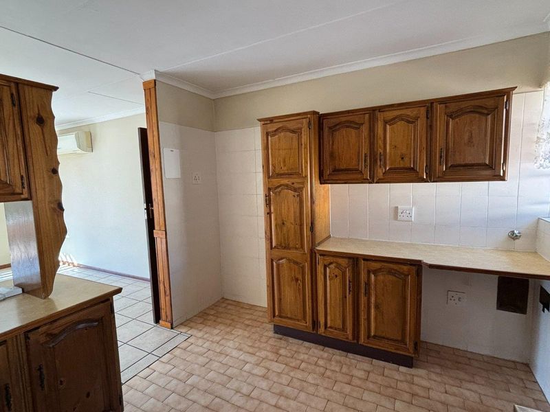 A functional kitchen area featuring traditional wooden cabinetry, tiled backsplash, and durable tiled flooring, offering a practical layout for daily use.